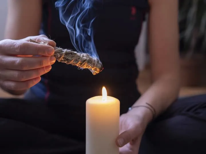 woman lighting smudge stick with candle