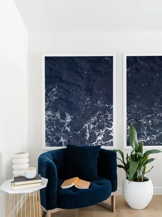blue accent chair in front of ocean artwork next to potted plant