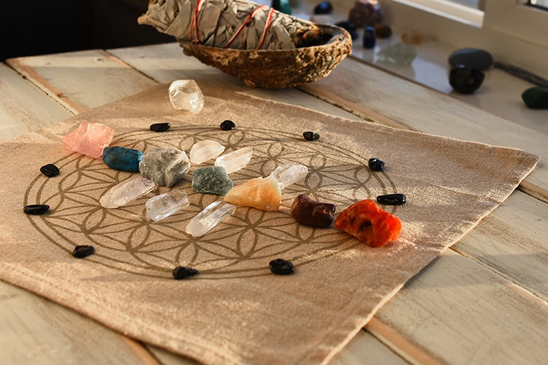 chakra healing crystal grid next to smudge stick in a dish
