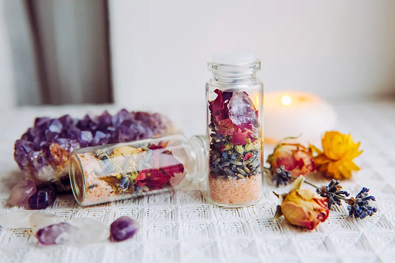 jars of dried flowers next to candles and amethyst crystals