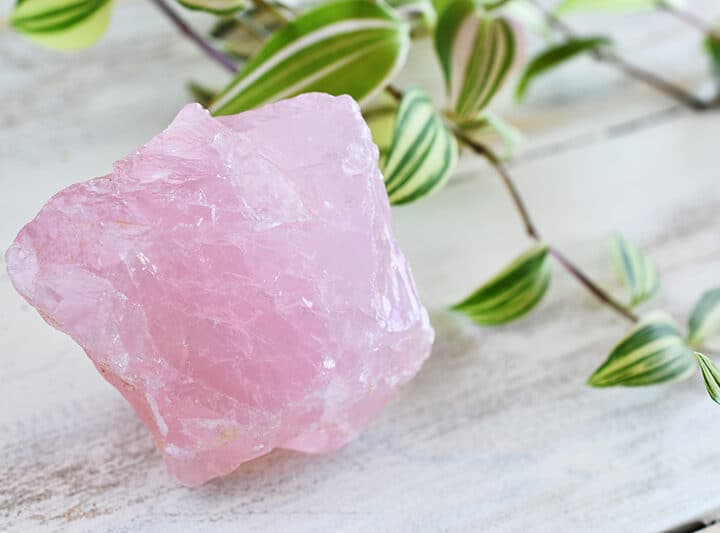 rose quartz crystal next to a plant
