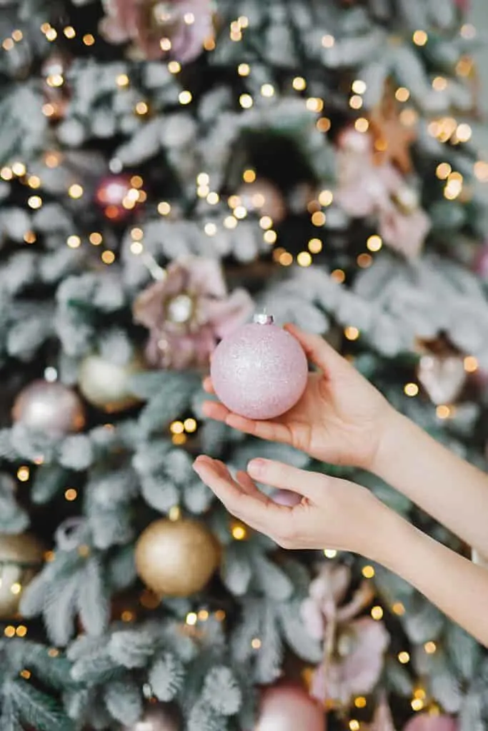 woman's hand holding Christmas ornament in front of a tree.