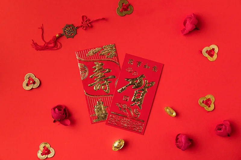 red envelope, three feng shui coins tied with red string, roses, and yuan bao