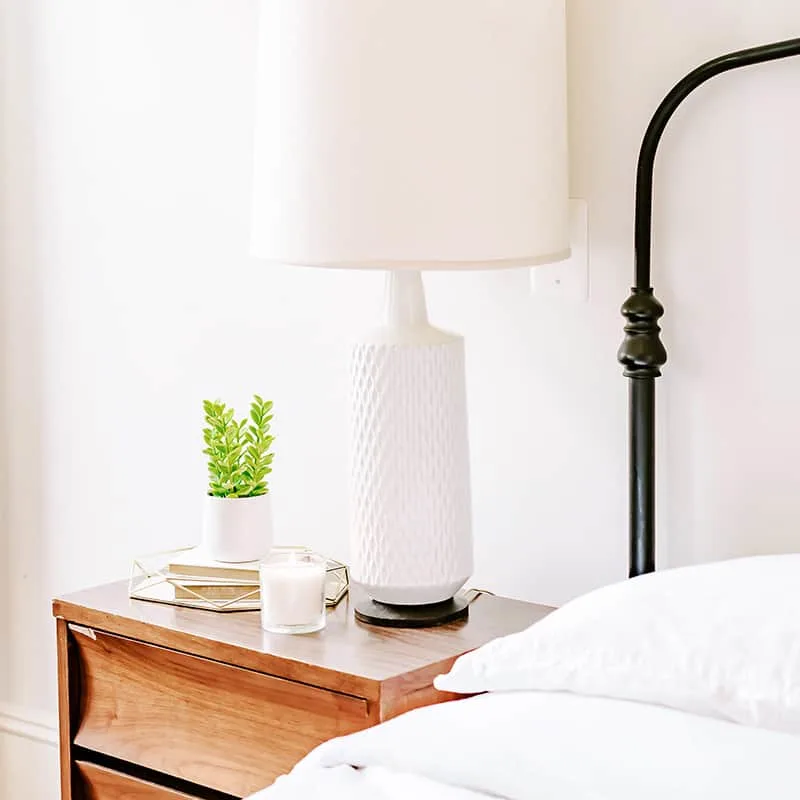 bedside table with lamp, candle, and small plant