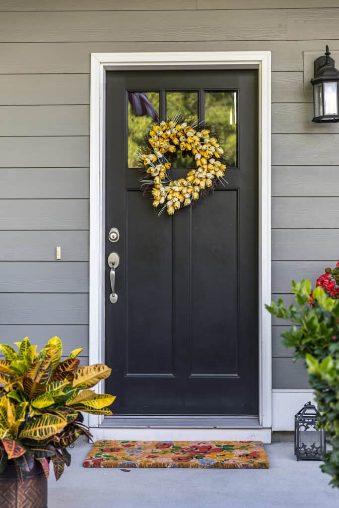 black front door with colorful wreath and doormat