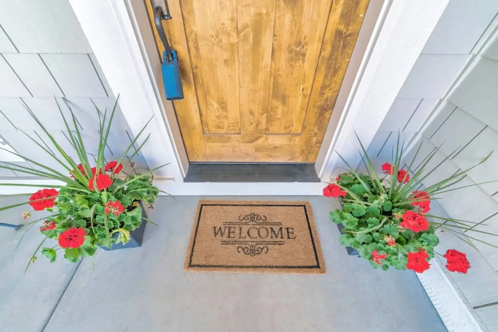 front door with welcome mat and red flowers in pots