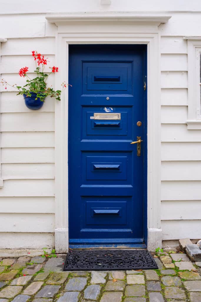 front door with good feng shui. blue front door, tidy welcome mat, flowers hanging next to door.