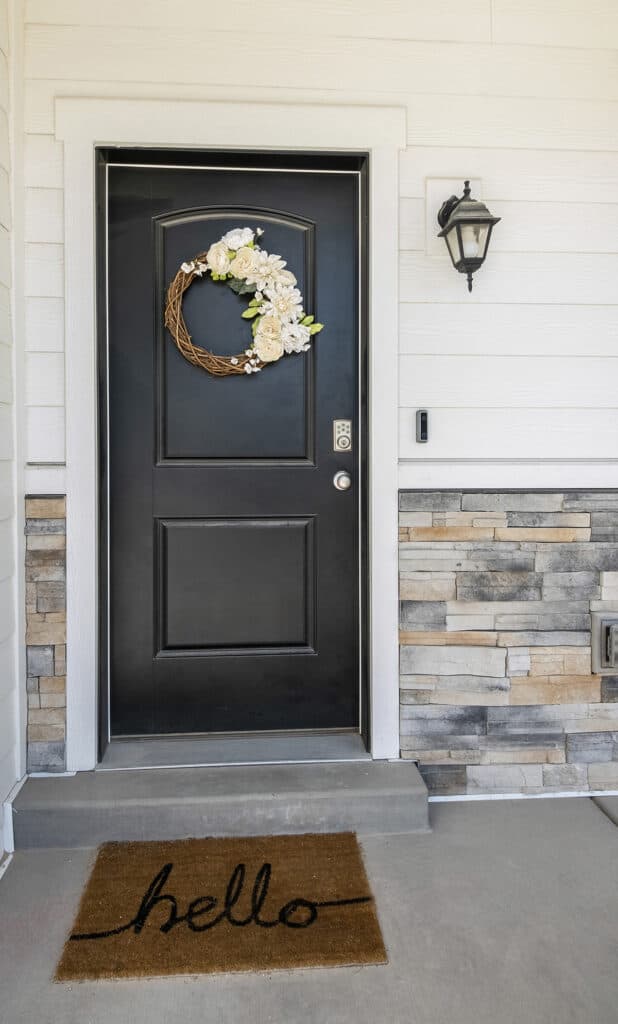 black front door with floral wreath and welcome mat that says "hello"